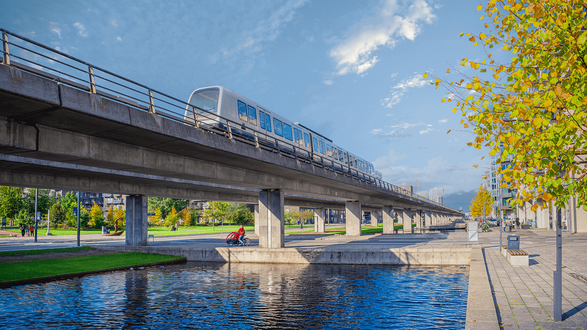 Metro kører på en bro i et grønt område nær Ørestad. 