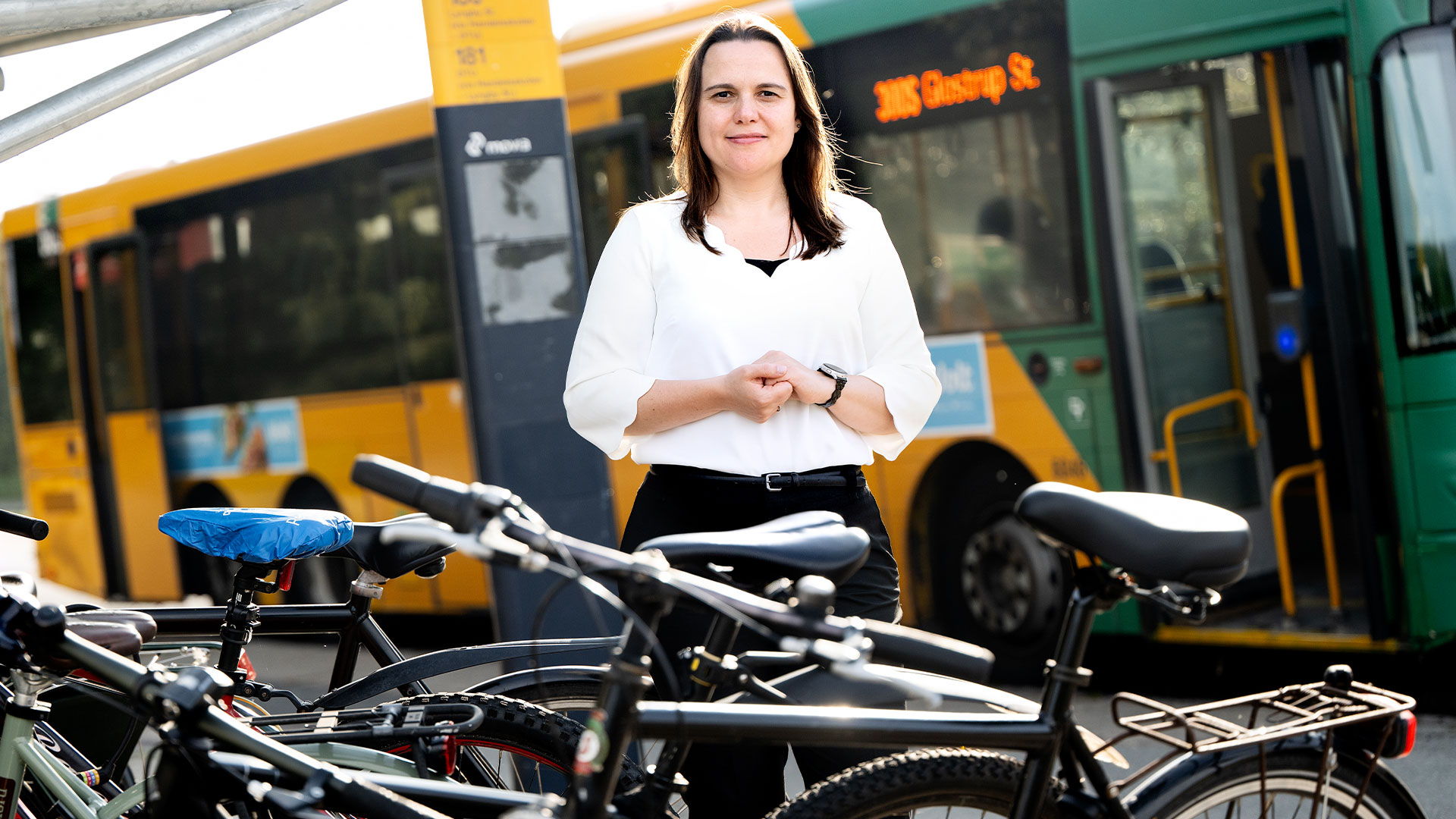 Kvinde står omringet af cykler foran en bybus. Foto: Bax Lindhardt