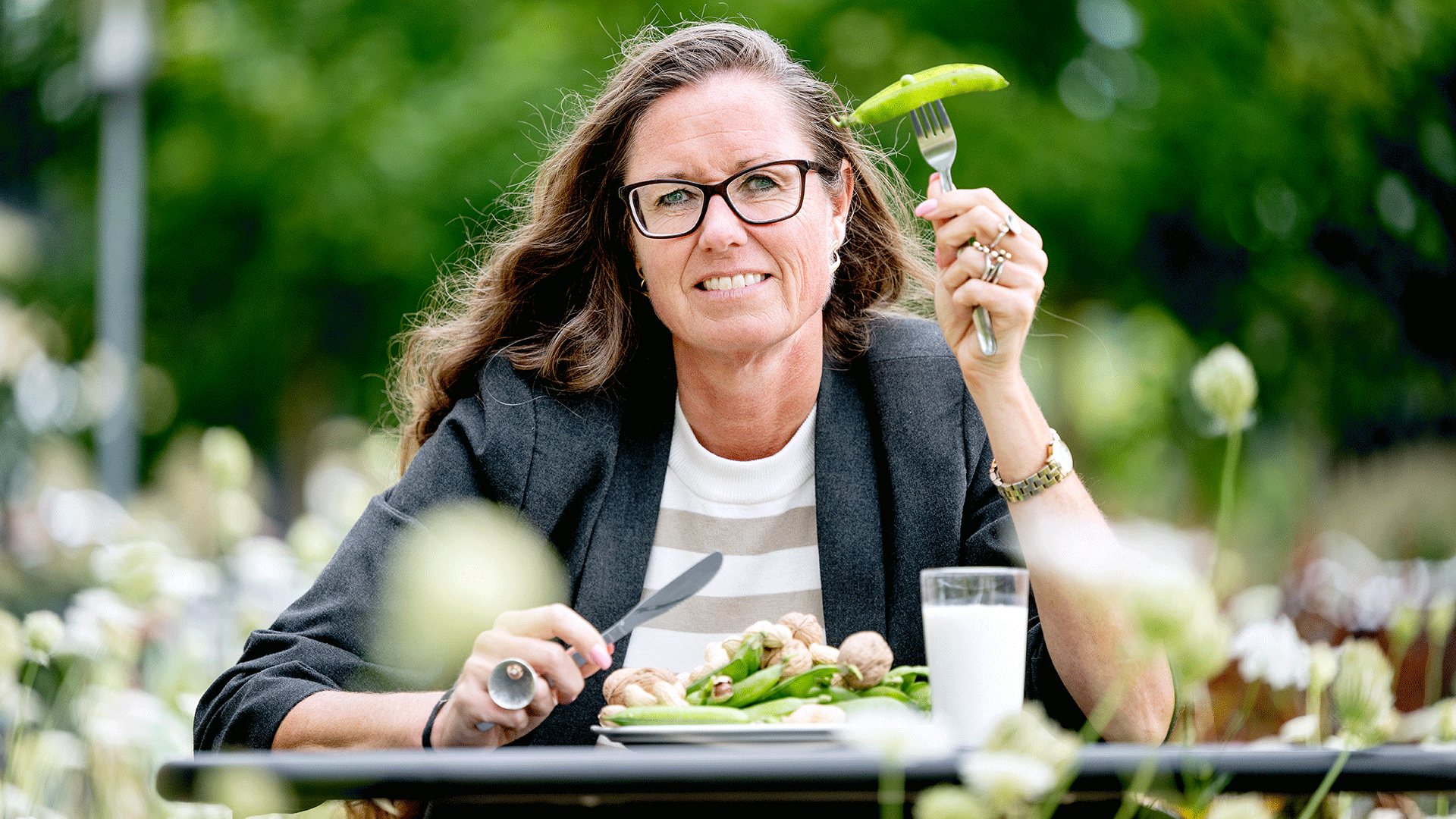 Kvinde siddende ved et bord med en tallerken og et glas, der indeholder fødevarer, som indeholder proteiner, der kan udløse allergi. 