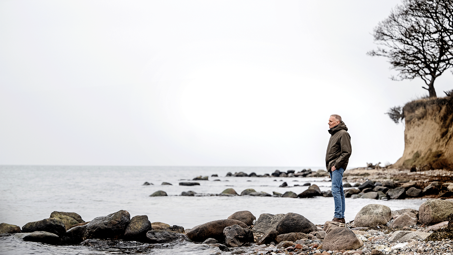 Professor Anders Baun står ved vandkanten nedenfor en skrænt og kigger ud over vandet.