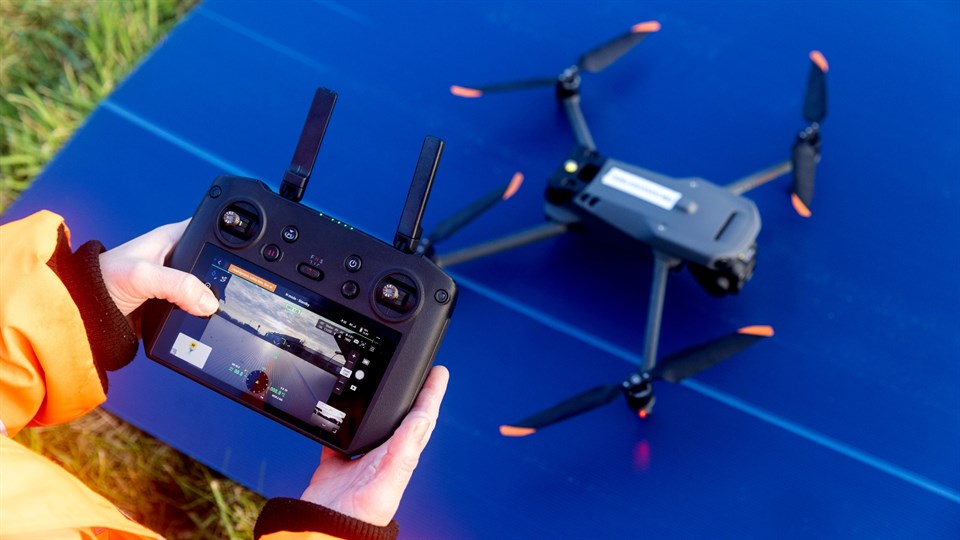 Hænder holder styringsinstrument ved siden af drone.