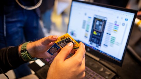 Closeup of someone holding a circuit board in front of a computer